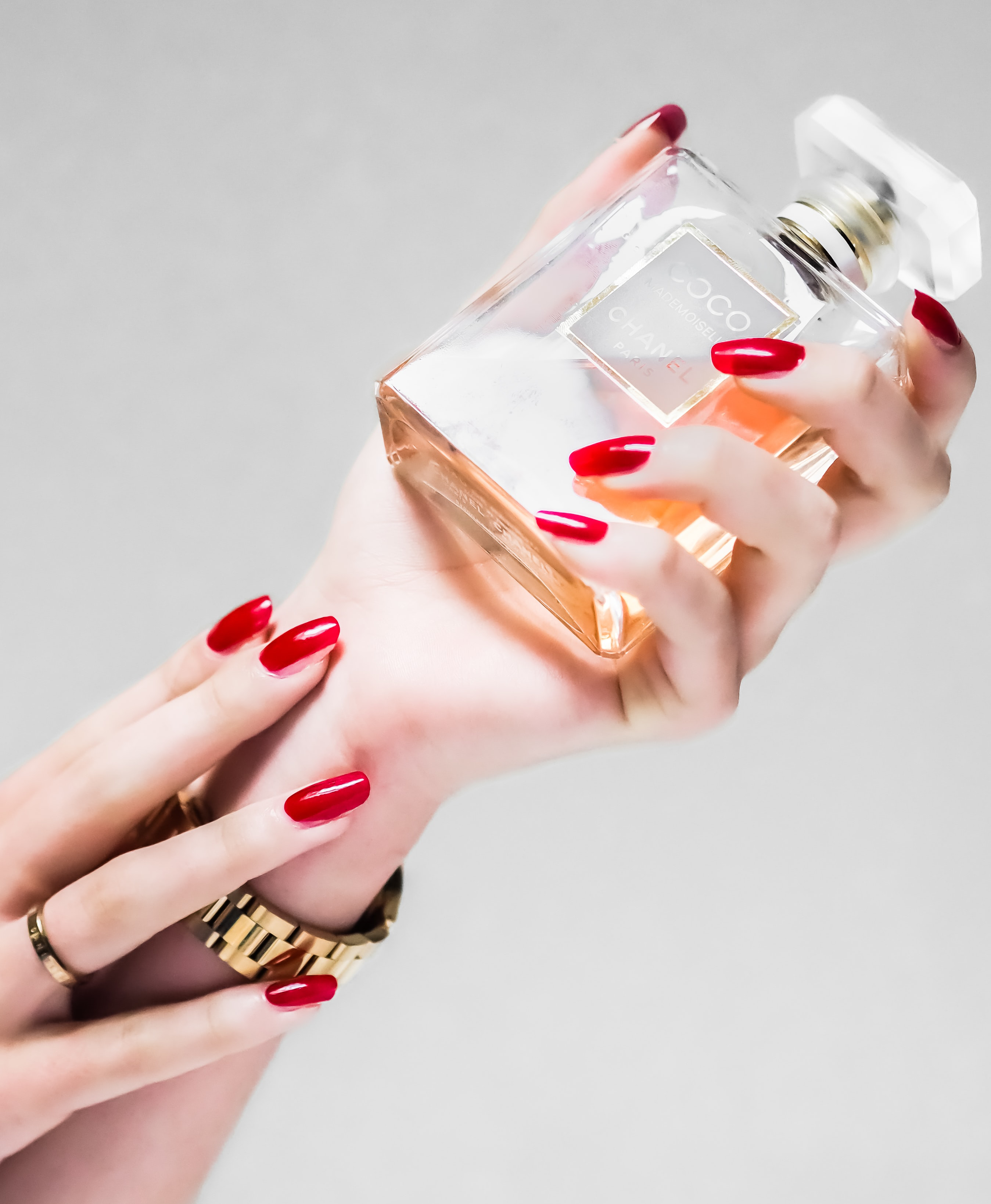 a photograph of someone with bright red nails holding a perfume bottle